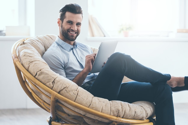 surfen op het web vanaf zijn tablet. zelfverzekerde jonge knappe man aan het werk op digitale tablet en glimlachen