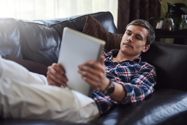 Surfen op zijn bank Hoge hoek opname van een knappe jonge man die zijn tablet gebruikt terwijl hij thuis op de bank zit