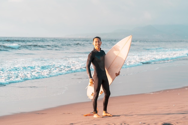 Surfer on the beach smiling with a surfboard and ocean background