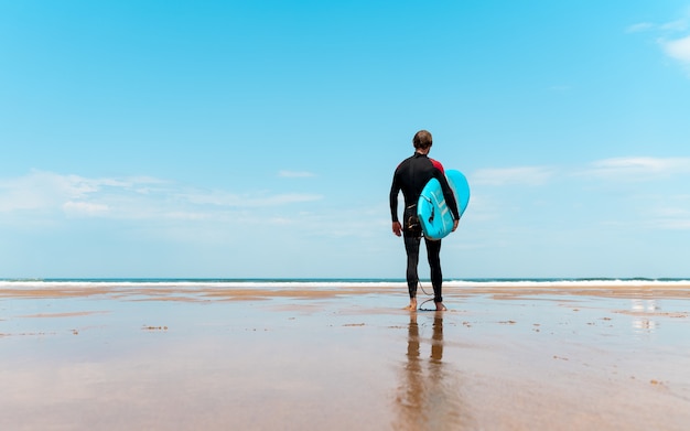 surfer on the beach with board in hand looking at the horizon and getting ready to surf