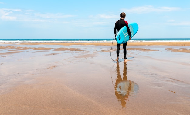 Surfer on the beach with board in hand looking at the horizon and getting ready to surf