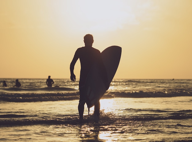 Foto surfista che trasporta la tavola in mare al tramonto