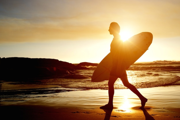 Surfer die op strand met surfplank loopt tijdens zonsondergang