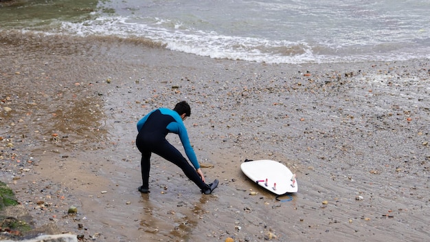 Foto surfer die zijn wetsuit aanpast op een kiezelstrand met surfplank kopieerruimte