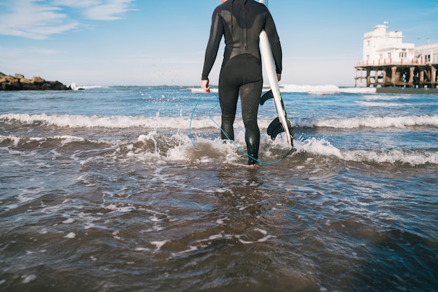 Surfer entering into the water with his surfboard.