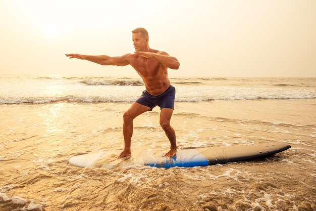 Surfer fitness male with a muscular body with his surfboard at the beach warm up