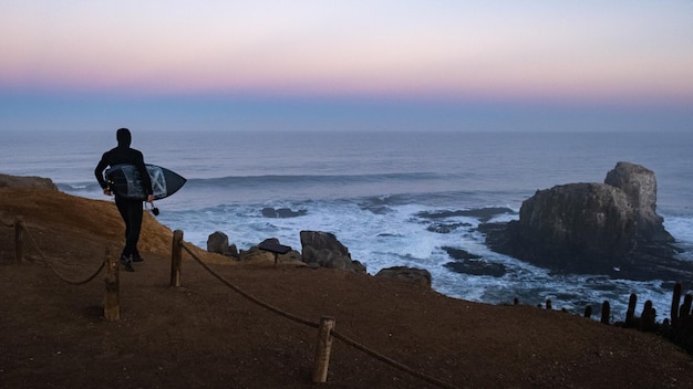Surfer gaat surfen, blauw uur, zwarte surfplank en wetsuit, zonsopgang in punta de lobos Pichilemu, Chili