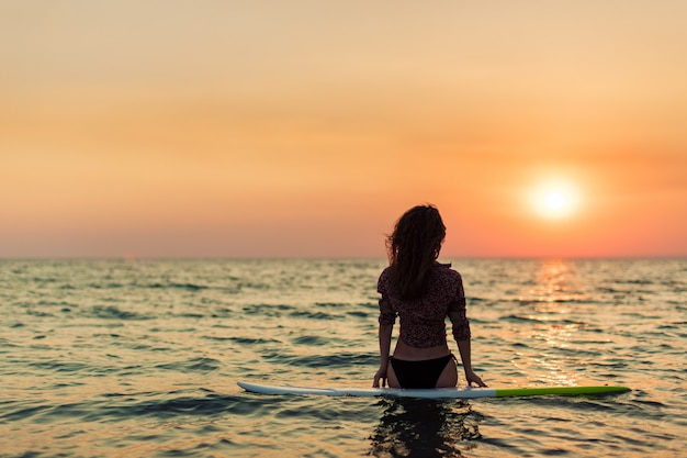 Surfer girl surfing looking at ocean beach sunset