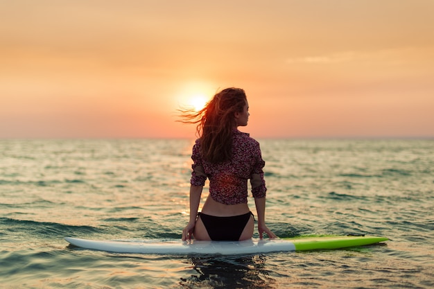 Surfer girl surfing looking at ocean beach sunset