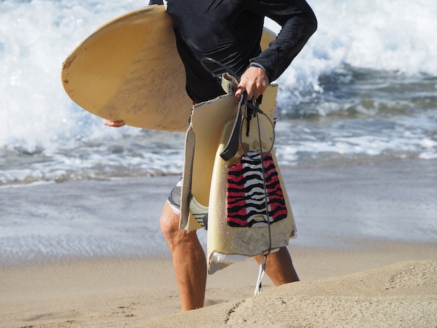 Il surfista va lungo la spiaggia con la tavola da surf rotta.