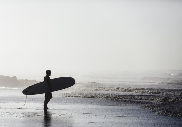 Photo surfer holding surfboard while standing on shore at beach