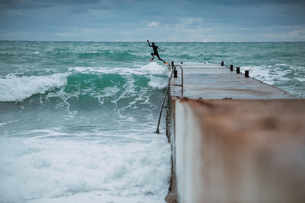 The surfer jumps into the sea from the pier to start catching the waves