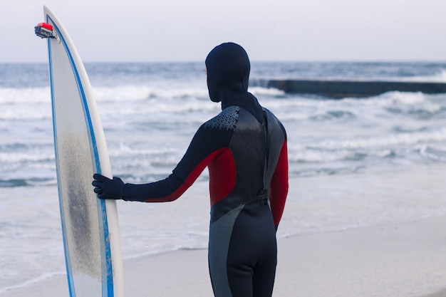 Surfer met surfplank staan. Hij draagt een wetsuit