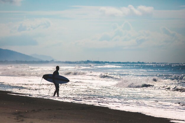 Photo surfer standing on beach by sea against sky