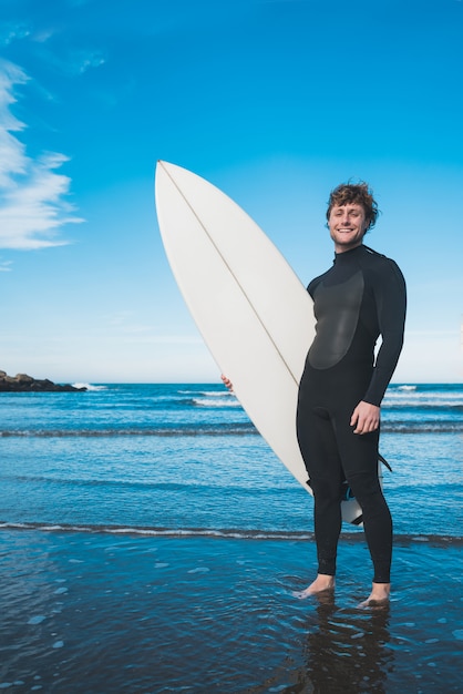 사진 그의 서핑 보드와 함께 바다에 서있는 서퍼.