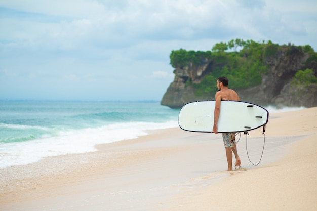 사진 서퍼. 모래 열 대 해변에서 산책하는 서핑 보드와 서핑 남자.