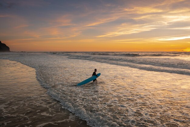 Surfer walking to ocean for sunset ride