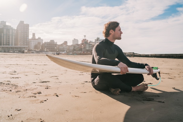 Surfer zittend op zandstrand met surfplank.