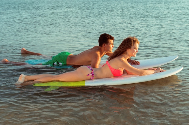 Surfing couple leaning on surfboards in sea