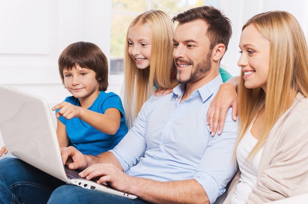 Foto navigare in rete insieme. vista laterale della famiglia felice di quattro persone che si legano l'una all'altra e sorridono mentre navigano in rete sul loro laptop