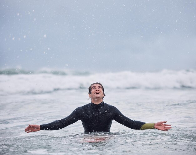 Surfing sports and man in ocean during rain enjoy nature spring weather and swimming in waves happiness raining and young male surfer in sea doing watersports for exercise training and fitness