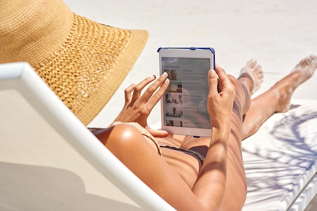 surfing in the sunshine cropped shot of a young woman using her tablet while relaxing at the beach