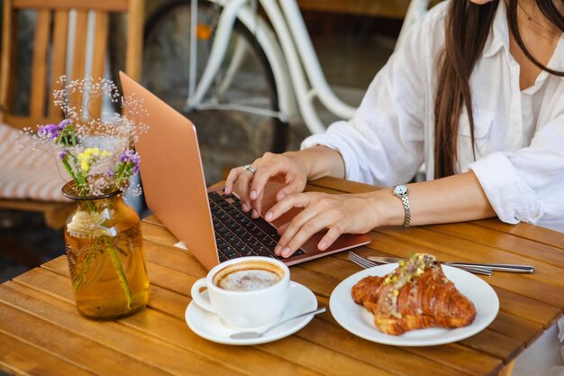 Photo surfing the web on a laptop in a summer cafe with a croissant and coffee