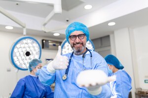 Хирург-врач улыбается, держа в руках хирурга силиконовый грудной имплантат.