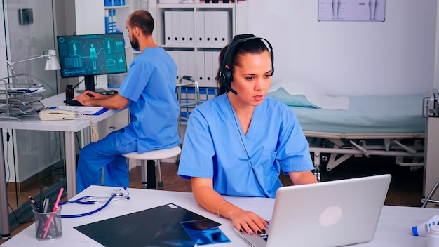 Surgeon assistant using headphones in hospital answering to patients calls for appointments and consultations. Healthcare physician in medicine uniform, doctor nurse helping with telehealth communicat