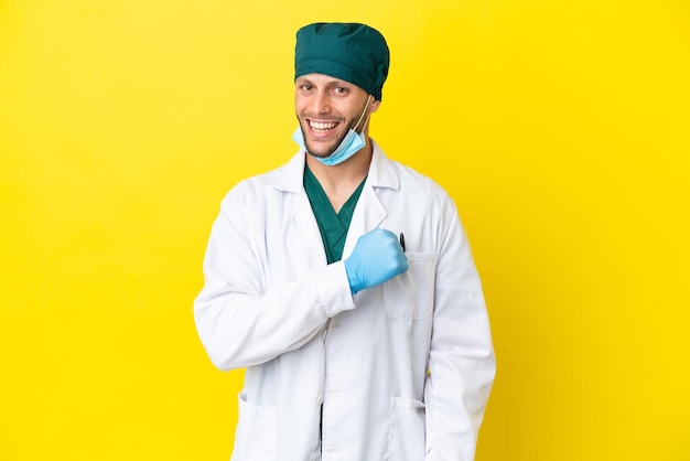 승리를 축하하는 노란색 배경에 고립 된 녹색 유니폼 외과 의사 금발 남자