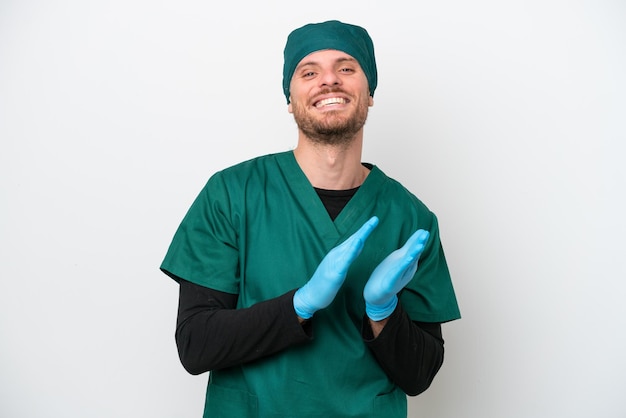 Бразильский хирург в зеленой форме на белом фоне аплодирует после выступления на конференции