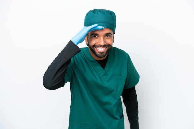 Surgeon Brazilian man in green uniform isolated on white background looking far away with hand to look something