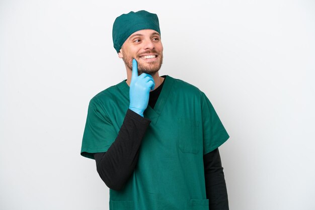 Surgeon Brazilian man in green uniform isolated on white background thinking an idea while looking up