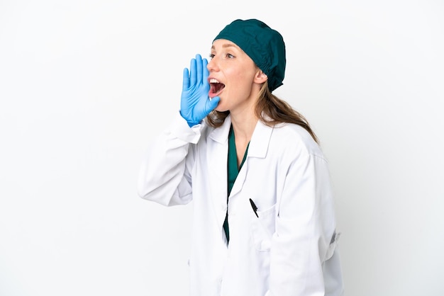 Surgeon caucasian woman in green uniform isolated on white background shouting with mouth wide open to the lateral