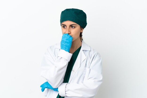 Surgeon caucasian woman isolated on white wall having doubts