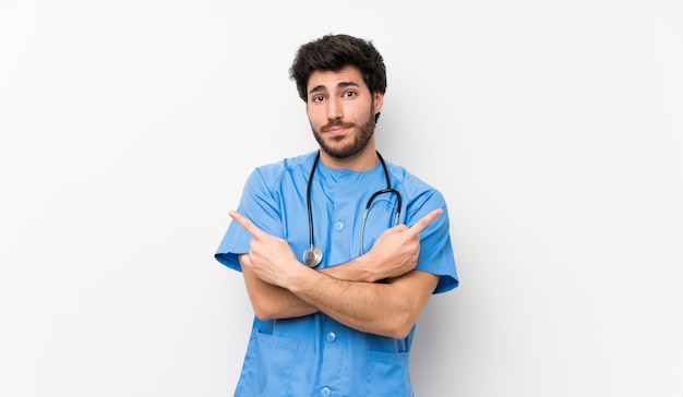 Surgeon doctor man over isolated white wall pointing to the laterals having doubts