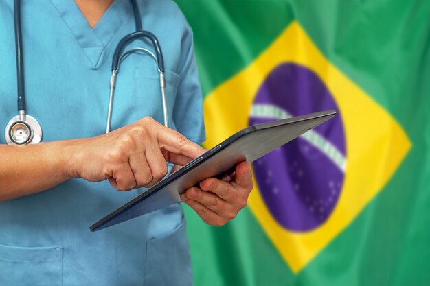 ブラジルの国旗の背景にデジタルタブレットを使用して外科医または医師