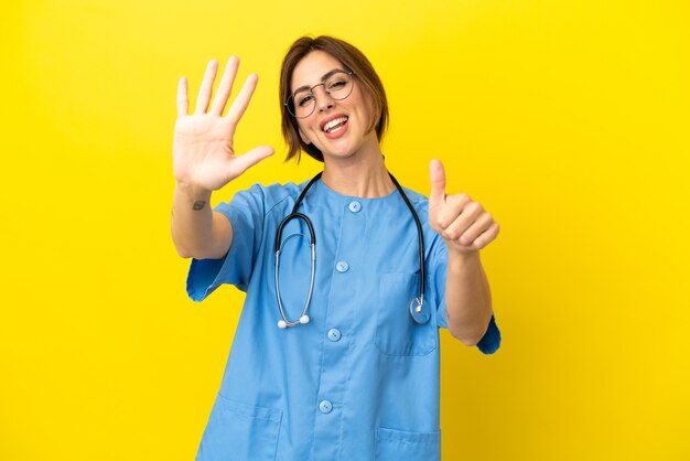 Surgeon doctor woman isolated on yellow background counting six with fingers