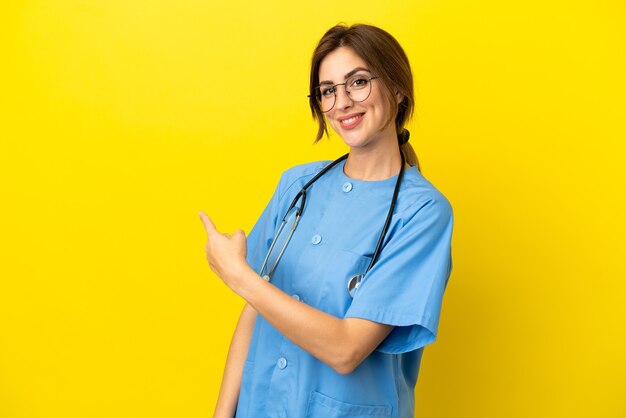 Surgeon doctor woman isolated on yellow background pointing back