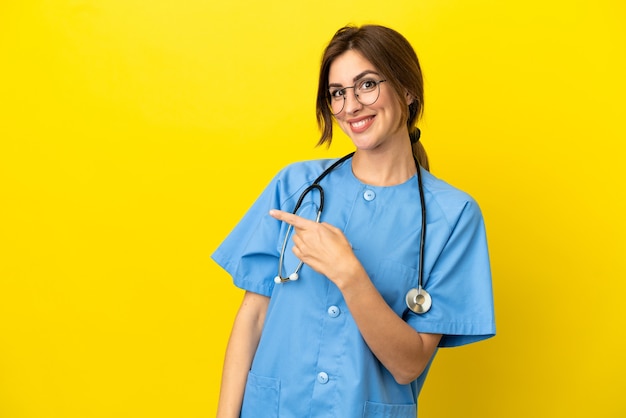 Женщина-врач-хирург изолирована на желтом фоне, указывая пальцем в сторону