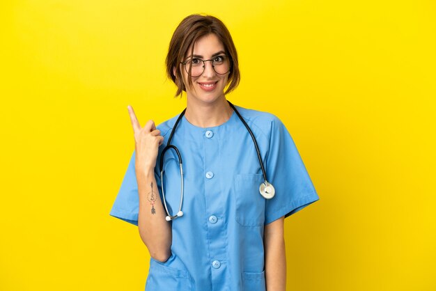 Surgeon doctor woman isolated on yellow background pointing to the side to present a product