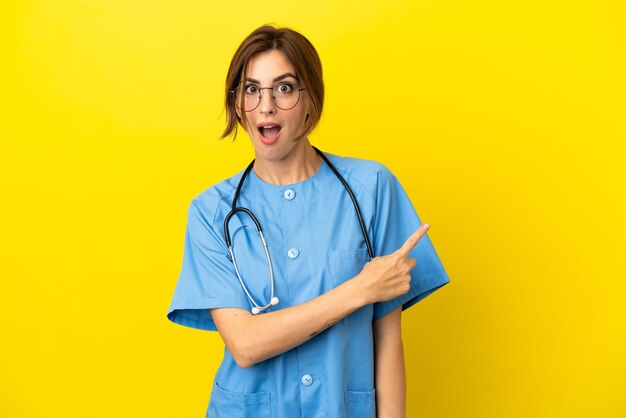 Surgeon doctor woman isolated on yellow background surprised and pointing side