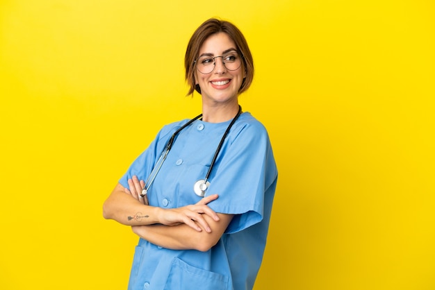 Женщина-врач хирурга изолирована на желтом фоне со скрещенными руками и счастлива