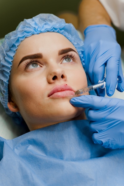外科医は魅力的な女の子のために診療所でフィラーを使用してプラスチック手術の唇の増強を行います