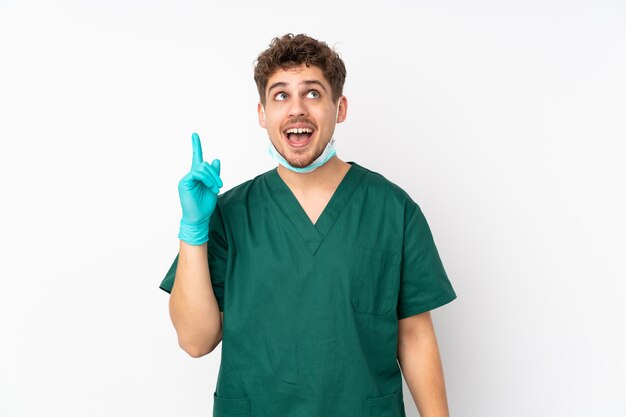 Surgeon in green uniform on isolated white wall pointing up and surprised