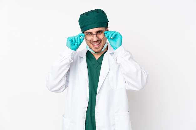 Surgeon in green uniform on white wall with glasses and surprised