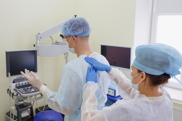 The surgeon is preparing for surgery an assistant helps an\
experienced surgeon to put on sterile clothes before surgery