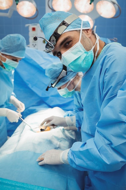 Surgeon looking at camera while colleagues performing operation