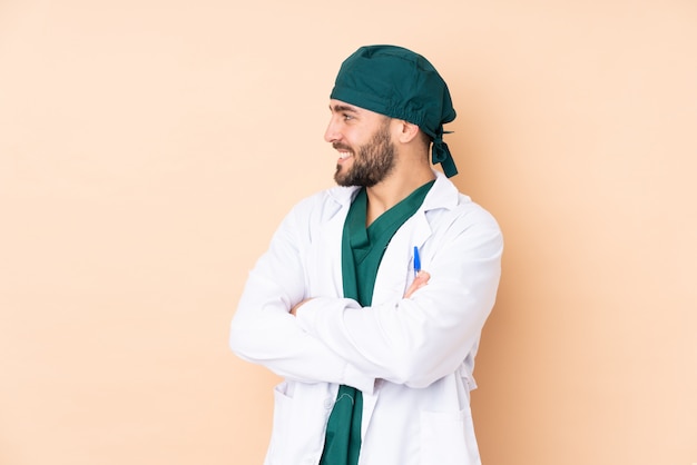 Surgeon man isolated on beige wall looking to the side