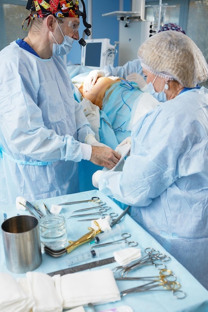 Хирург и медсестра готовятся к операции в операционной. Надевают халаты, шапки и маски. Настраивают оборудование, освещают, готовят стерильные простыни.